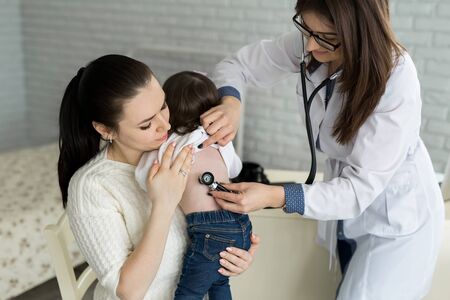 Professional general medical pediatrician doctor in white uniform gown listen lung and heart sound of child patient with stethoscope: Physician check up kid female after consult in hospital.の写真素材