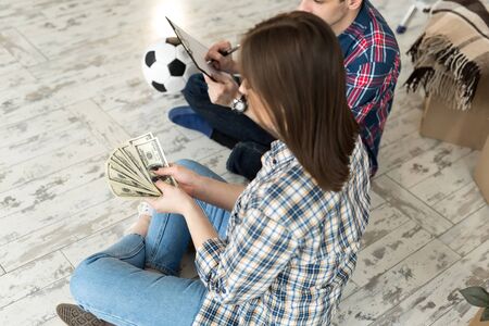 Young couple counting money while sitting on floor in new apartmentの写真素材