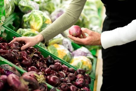 Closeup of young woman hand pick up onion on the basket in the supermarket.の写真素材