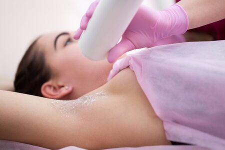 Cosmetologist sprinkles talcum powder on a young girl's armpit before the depilation procedure. The girl lies on a couch in a beauty salon, she does the procedure shugaringの写真素材