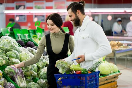 Portrait of a healthy couple looking at fruits and vegetables in the supermarket while shopping. Beautiful couple chooses cabbage in a supermarket.の写真素材