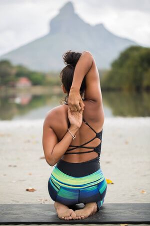 Young woman practices yoga on the shore of the Indian ocean in Mauritius and mountain in the background.の写真素材