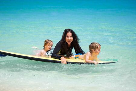 Twins, boy and girl with mom surfing in the ocean on a blackboard.