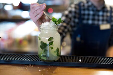 The bartender decorates the Mojito cocktail with lime and mint