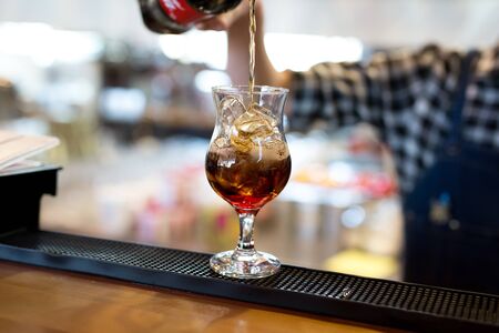 The bartender in the restaurant pours Cola into a cocktail glass