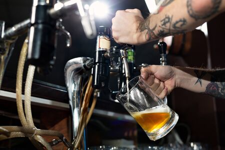 Draft beer pour in a glass from the crane. Waiter pours beer in a pub.の写真素材