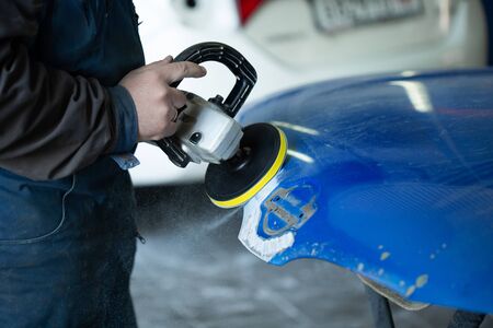 A man who sanding with a grinder and prepares the paint for the car in a car service. Repairman fix...