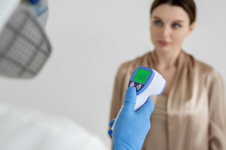 Infectious disease doctor measures the temperature of a woman patient with an infrared thermometer...