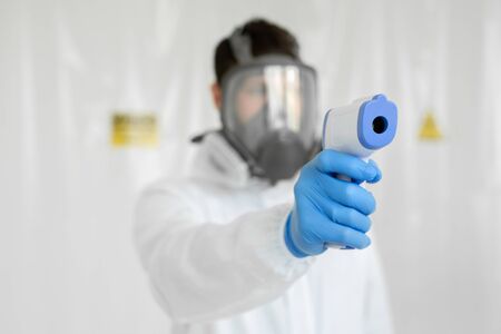 Close-up shot of doctor wearing protective respiratory mask ready to use infrared forehead thermometer gun to check body temperature for virus symptoms epidemic virus outbreak concept coronavirusの写真素材