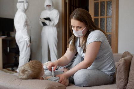 Mom measures babys temperature. Doctors in protective suits at sick patients at home. Coronavirus, covid-19の写真素材