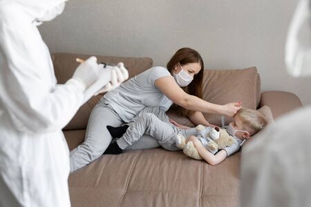 Mom measures babys temperature. Doctors in protective suits at sick patients at home. Coronavirus, covid-19の写真素材