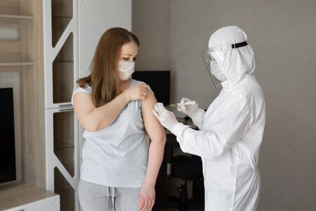 Doctor in personal protective suit or PPE inject vaccine shot to stimulating immunity of woman...
