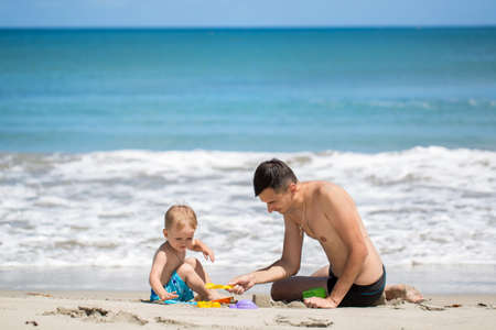 father and son building sand castle on beach.の写真素材