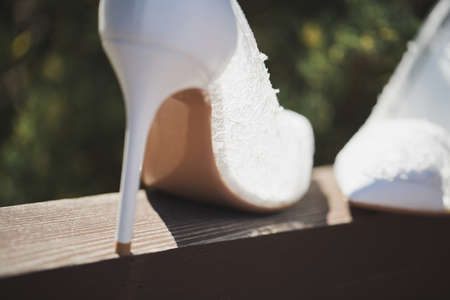 Elegant white wedding shoes on a wooden beam on the background of the pool