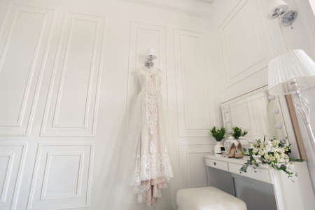 Elegant wedding white dress hanging on a wall during a wedding preparation. Brides morning. Before ceremony.の写真素材