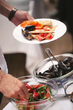 A mans hands put sea products on a plate at a buffet