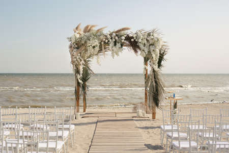 Outdoor area for beach ceremonies with sea view, white chairs, flower arch on a sunny day.の写真素材
