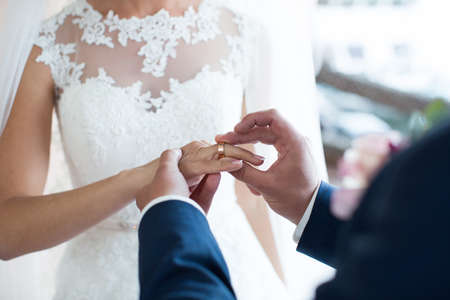 The groom puts a ring on the brides finger during the wedding ceremony.の写真素材