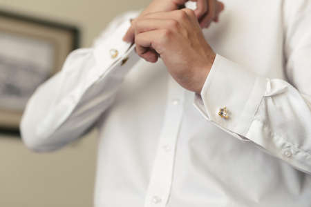 Men put on a shirt and fasten cufflinks on the morning of the wedding day