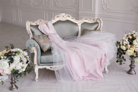 Luxurious pink wedding dress is lying on a grey sofa in a white room.の写真素材