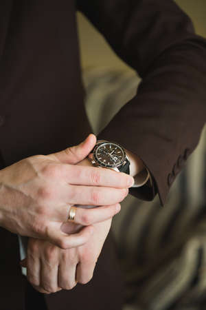 Close-up hands of the groom with a clock.