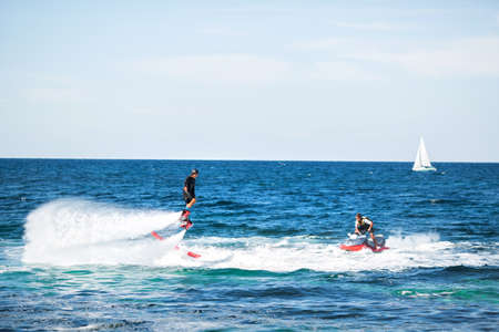A rider on a flyboard in the ocean does difficult stunts.