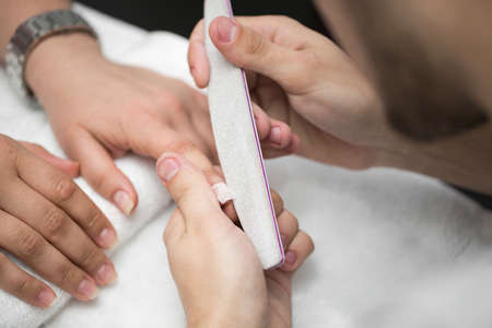 Man manicurist doing manicure for women in beauty salon.の写真素材