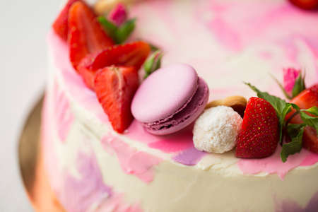 Beautiful cake with strawberries and macaroons on a white table.の写真素材