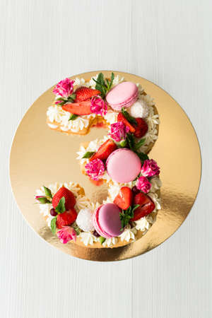 The cake with cheese cream and honey cakes is decorated with flowers, berries and sweets. A cake in the shape of the number 3の写真素材