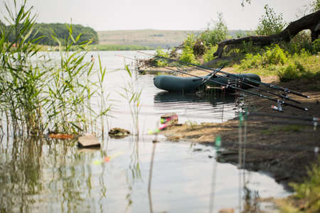 An inflatable boat, with boxes with fishing tackles, is standing on the water, pond, lake, near the...