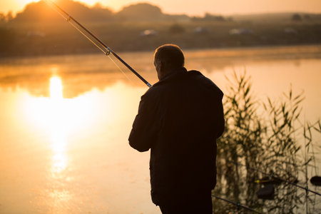 The angler fishing with spinning on the pond, the lake at sunset.の写真素材