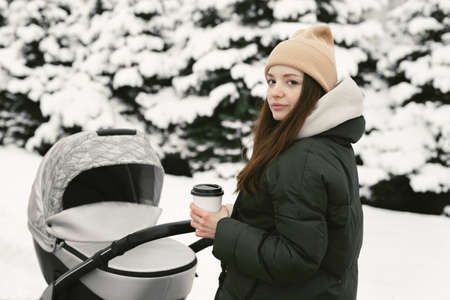 Portrait of a young beautiful woman with a stroller in a snowy park in winterの写真素材