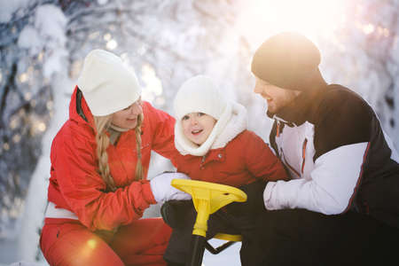 Portrait of a happy family in winter in the forest. The son is sitting on a sled, and dad and mom hug him and laughの写真素材