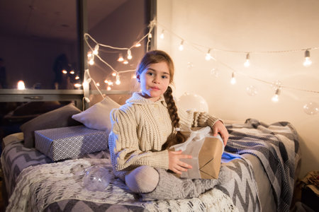 Beautiful little girl sitting on bed with a gift in its hands.