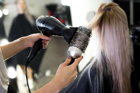 Drying long blonde hair with hair dryer and round brush.の写真素材