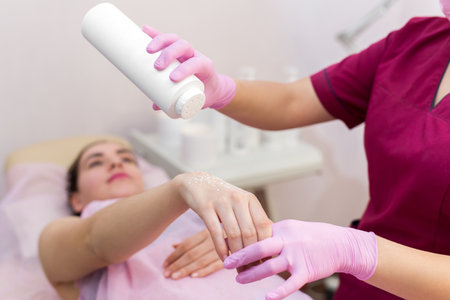 Close-up of a beautician sprinkles talcum powder on a young girls hand before the depilation procedure. The girl lies on a couch in a beauty salon, she does the procedure shugaring.の写真素材