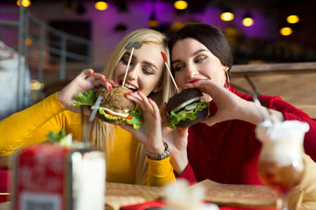 Two happy girls bite burgers. Concept of fast food.