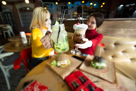 Young women toasting cocktail glasses in a cafe.