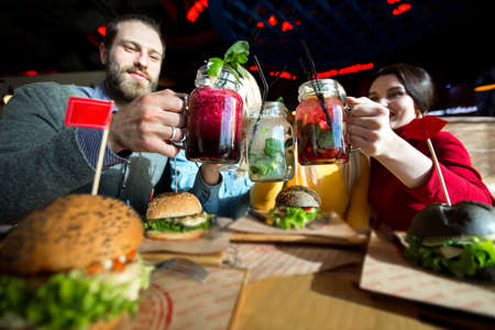 People have dinner together at a table in a cafe. Happy friends clink glasses with cocktails and laughの写真素材