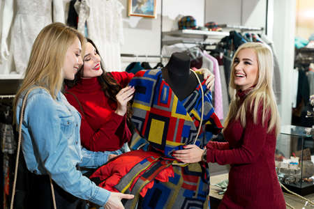 Shopping, fashion and friendship concept - three smiling friends trying on some clothes at shopping mallの写真素材