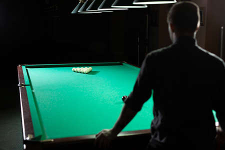 A man plays Billiards. The view from the back.