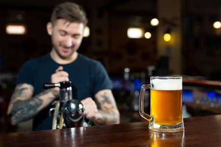 Bartender pouring from tap fresh beer into the glass in pub.