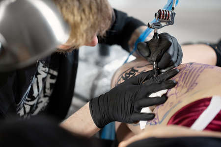 Close up image of the bearded tattoo male artist makes a tattoo on a female leg.の写真素材