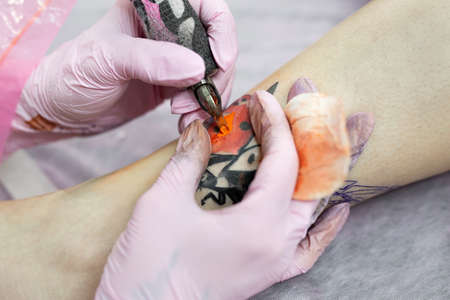Needle tattoo machines inject a red ink into the skin of a girl. Close-up of the process of applying the tattoo on the skin.の写真素材
