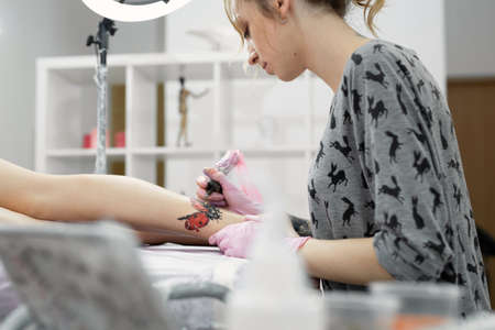 Professional tattoo artist which making tattoo on the leg of a young girl. Hands of a tattoo artist. Tattooist makes a tattoo.の写真素材