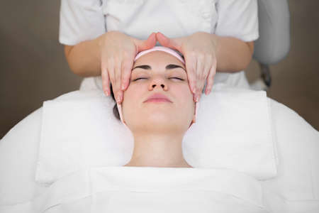 Beautician makes a professional massage of the face of the neck and shoulders for a young girl in the Spa salon. The view from the top. Facial beauty treatment.の写真素材