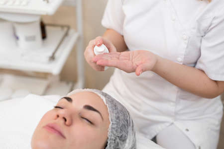 Hands of beautician apply cream to face of woman. Concept of beauty and youth. Close-up beautician causes moisturizer on the girls face.の写真素材