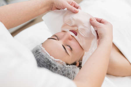 Beautician removes a clay mask from the face of a young girl in the Spa salon. Beautiful young girl at the beautician does the spa proceduresの写真素材