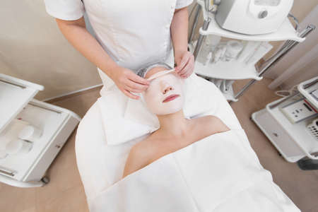 Beautician removes a clay mask from the face of a young girl in the Spa salon. Beautiful young girl at the beautician does the spa proceduresの写真素材