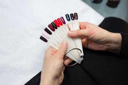 Manicure and nail care concept. A woman in a beauty salon holds colored test nail polishes with different colors and chooses the color for paintingの写真素材